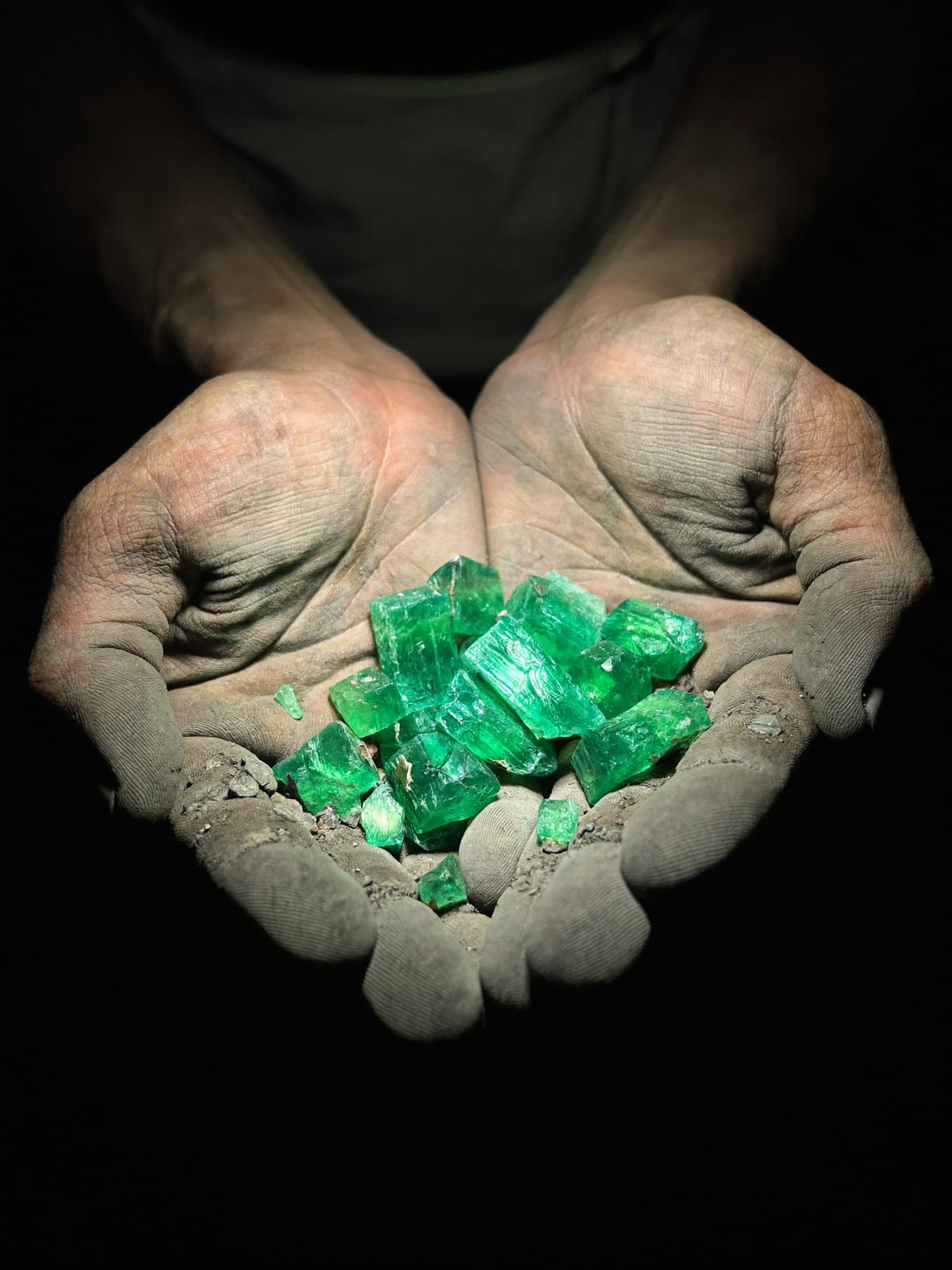 Manos ahuecadas sosteniendo un puñado de cristales de esmeralda en bruto