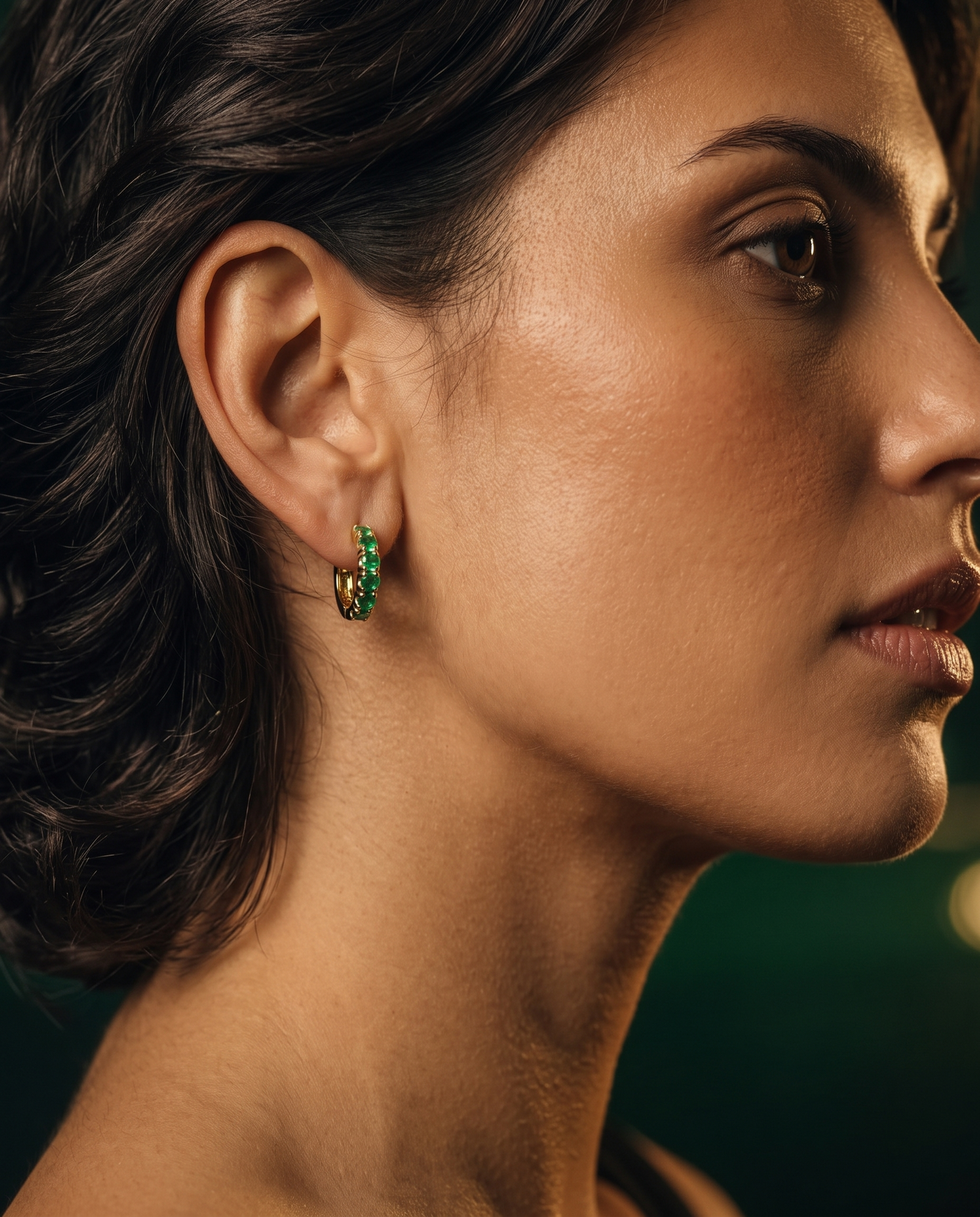 Modelo de perfil con una candonga de esmeralda puesta, sobre fondo oscuro